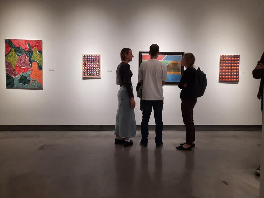 Three students standing and talking at an art exhibit.