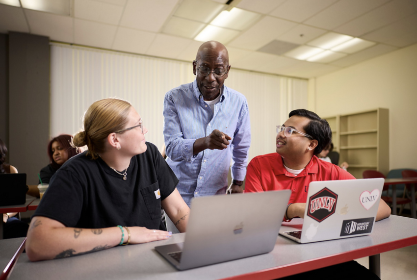 A professor talking to two students on laptops