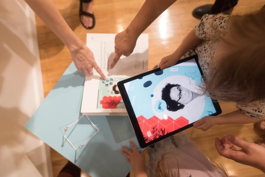 Close up shot of students gathering around an iPad and a piece of art