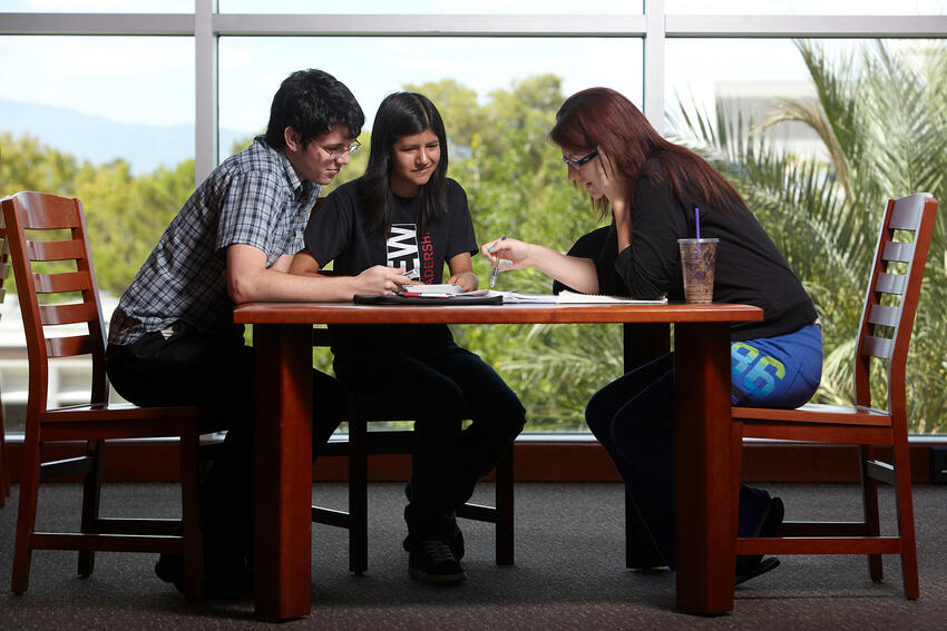 Three students study together at table in library