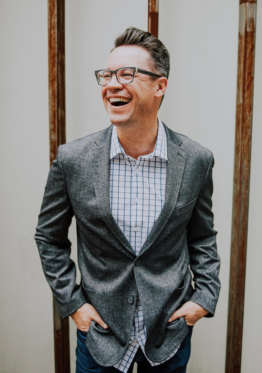 A smiling man with glasses in a gray suit.