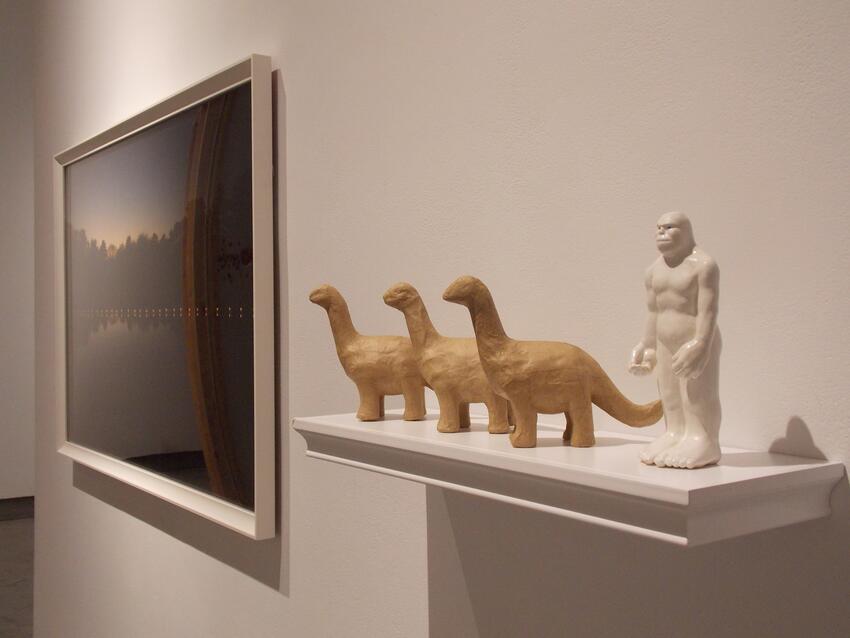 Small sculptures of dinosaurs and a model gorilla sitting on a shelf, a piece of framed art hangs on the wall.