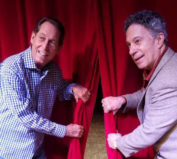 Two men pulling back a red curtain.