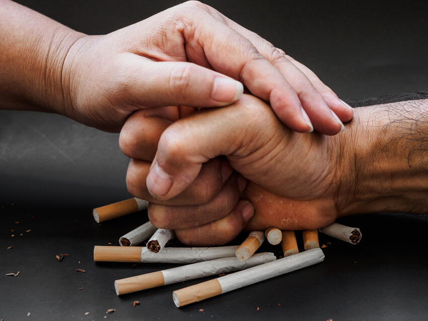Hand of one person preventing another person from picking up a cigarette