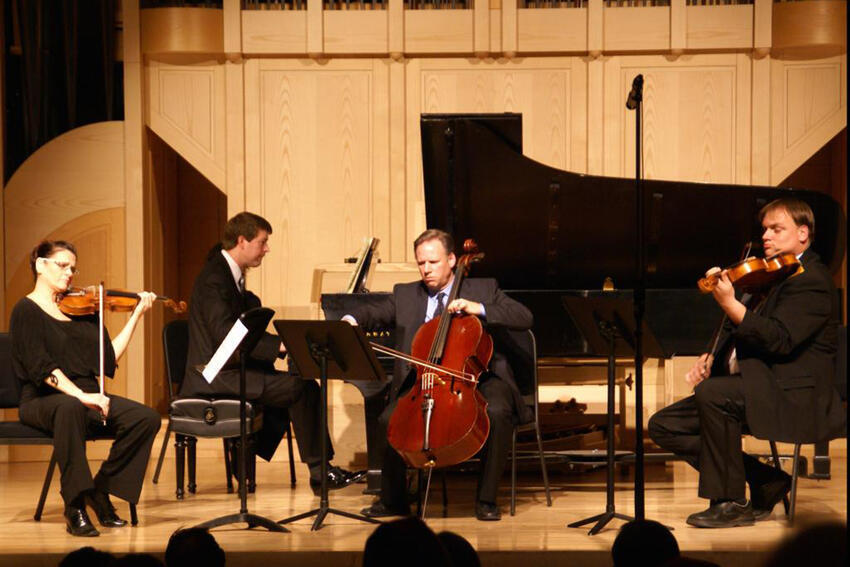 A violinist, pianist, cellist, and violist performing on stage