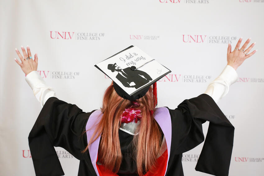 A College of Fine Arts graduate faces a backdrop (with her back to the camera). She's wearing her gown and mortarboard. The mortarboard has an image of Frank Sinatra with the words, &quot;I did it my way.&quot;