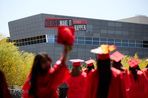 eight UNLV graduates walking in their cap and gowns with the sign &quot;rebels make it happen&quot; afar