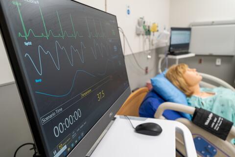 A heart rate monitor on a table with a mannequin resting on a bed