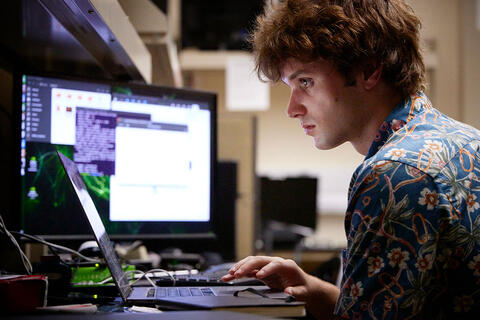 A man looking at a laptop with a monitor screen in the background.