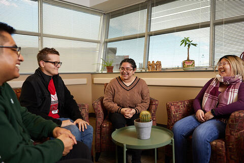 Four people sit together, smiling and talking in a room with plants and a cactus on the table.