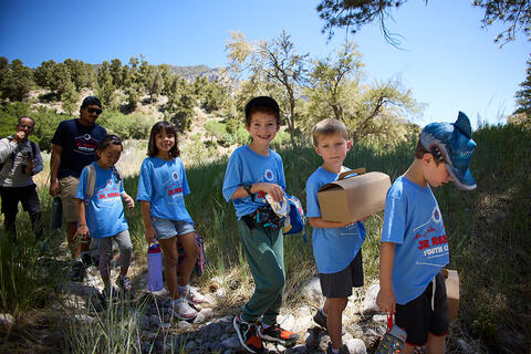 A group of young children walking along a trail surrounded by trees and natural scenery.