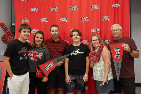 A family holding UNLV props in front of a drop board with the words "U-N-L-V"