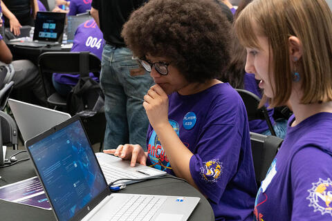 Two kids looking at laptop screens at a table