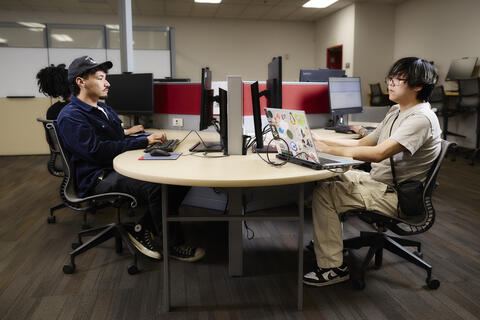 2 students sitting at a table looking at computers