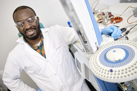 A student in a lab wearing a white coat and blue gloves