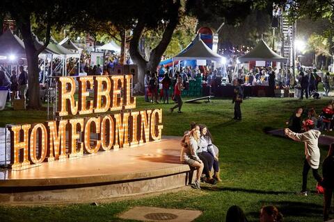 Two students taking a photo by the Rebel Homecoming sign