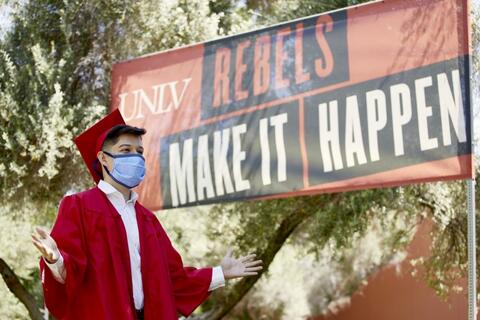 Graduate with mask in front of Rebels Make it Happen sign