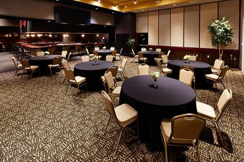Large indoor event space with six evenly spaced round table with dark blue tablecloths and six white chairs around each table