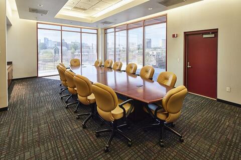 Large wood conference table surrounded by large plush office-style chairs, the back corner of the room has floor to ceiling windows overlooking the Las Vegas Strip
